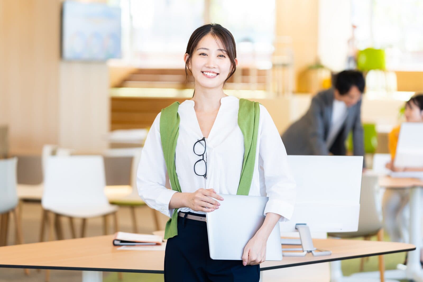 明るいオフィスでノートパソコンを手に微笑む女性社員